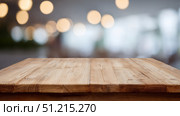 A rustic wooden tabletop is positioned prominently in the foreground, with a softly blurred backdrop of warm, glowing bokeh lights suggesting a cozy indoor setting. The natural texture and grain of the wood are clearly visible, lending an authentic and earthy feel to the scene. The soft focus in the background evokes a welcoming atmosphere, potentially in a restaurant, café, or home kitchen. This image can be used to emphasize warmth, hospitality, culinary experiences, or product display in a comforting and intimate environment. Стоковое AI-изображение, AI-художник Ксения Чунаева / Фотобанк Лори
