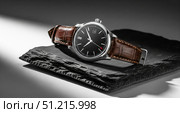 Luxury men's watch with black dial and brown leather strap, classic analog wristwatch on black slate stone, elegant male accessory. Стоковое AI-изображение, AI-художник Павел Муравьев / Фотобанк Лори