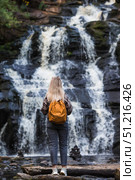 Tourism. Hiking. A young woman with a backpack on her back stands in front of the Yukankoski Waterfall (White Bridges) in the Republic of Karelia. Стоковое фото, фотограф Photojuli / Фотобанк Лори