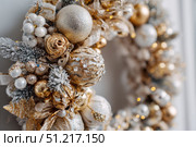 Delicate wreath of golden Christmas decorations hangs on the white wall. Magic and joy festive celebrations during the winter season. Elegant gold and silver Ornaments beautifully decorated setting. Стоковое AI-изображение, AI-художник Марина Демидюк / Фотобанк Лори