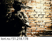 Special forces fighter standing against a brick wall, armed with thermal imaging device on helmet and submachine gun. Стоковое фото, агентство ТАСС / Фотобанк Лори