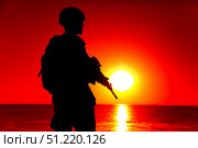 Silhouette of rifleman standing on ocean coastline, patrolling at sunset. Oleg Zabielin / Stocktrek Images/TASS. Стоковое фото, агентство ТАСС / Фотобанк Лори