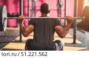 Muscular athlete performing weighted squats, holding heavy barbell across shoulders during intense strength workout in contemporary fitness facility, demonstrating physical discipline. Стоковое AI-изображение, AI-художник Юрий Поздников / Фотобанк Лори