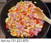 Diced chicken and vegetables are being stir-fried in a cast-iron pan with a wooden spoon. Concept of: Culinary preparation. Стоковое фото, фотограф Ольга Петрова-Апостолова / Фотобанк Лори