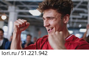 Sports enthusiast in red shirt jubilantly celebrating team win, raising fists with electric excitement amid roaring stadium crowd. Стоковое AI-видео, аниматор Юрий Поздников / Фотобанк Лори