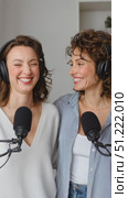 Smiling female radio broadcasters laughing during podcast recording, wearing headphones while producing entertaining audio content. Стоковое AI-видео, аниматор Юрий Поздников / Фотобанк Лори