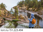 Tourism. Hiking. Ladoga skerries on Lake Ladoga. A female tourist in a raincoat with a backpack on the rocky islands looks into the distance. Republic of Karelia, Russia. Стоковое фото, фотограф Photojuli / Фотобанк Лори