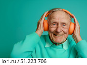 Улыбающийся пожилой мужчина в оранжевых наушниках слушает музыку на бирюзовом фоне. Стоковое AI-изображение, AI-художник Кирилл Сиротюк / Фотобанк Лори