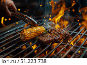 Аппетитный говяжий стейк и початок кукурузы жарятся на решетке барбекю с дымом и пламенем. Стоковое AI-изображение, AI-художник Кирилл Сиротюк / Фотобанк Лори