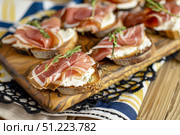 Изысканные закуски с прошутто, сливочным сыром и зеленью выложены на деревянной сервировочной доске. Стоковое AI-изображение, AI-художник Кирилл Сиротюк / Фотобанк Лори