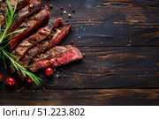 Нарезанный стейк средней прожарки, украшенный веточками розмарина и помидорами черри, лежит на темном деревянном фоне. Стоковое AI-изображение, AI-художник Кирилл Сиротюк / Фотобанк Лори