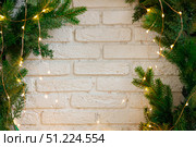 Christmas fir branches decorated with garland on brick wall. Стоковое фото, фотограф Aleksandra Selivanova / Фотобанк Лори