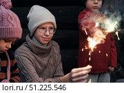 Children celebrating with colorful sparklers while dressed in warm clothing attire. Kids siblings enjoy the winter holidays outdoors. Festive evening. Christmas. New Year. Family Milestone Celebration. Стоковое фото, фотограф Марина Демидюк / Фотобанк Лори