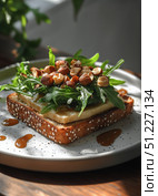 Delicious Open-Faced Sandwich Topped With Fresh Greens and Nuts Served on a Wooden Table. Стоковое AI-изображение, AI-художник Юлия Гапеенко / Фотобанк Лори