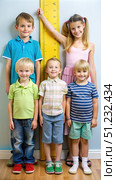 Four Children Standing Next to a Yellow Height Meter in a Room. Generative AI. Стоковое AI-изображение, AI-художник Roman Zavorotny / Фотобанк Лори