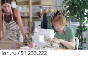 Young dressmaker draws with curved rulers on paper, she designs patterns once while a mature female seamstress works on a sewing machine. Стоковое видео, видеограф Яков Филимонов / Фотобанк Лори