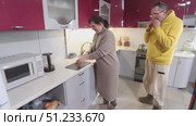 Eating orange slices with peel middle aged white couple stand in modern kitchen surrounded by appliances and bright lighting creating warm atmosphere. Стоковое видео, видеограф Владимир Григорьев / Фотобанк Лори