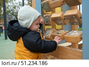 Маленький ребёнок играет на детской площадке, мальчик передвигает деревянные фигурки, подвешенные на металлической трубке. Малыш одет в шапку, куртку и джинсы, ему 8 месяцев. Стоковое фото, фотограф Яна Проничева / Фотобанк Лори