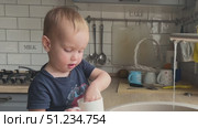 A joyful child is happily playing with water in the kitchen sink, exploring and having fun. Стоковое видео, видеограф Olesia Kondrateva / Фотобанк Лори