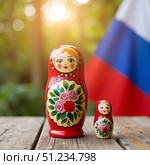 На деревянном столе стоит ярко разукрашенная русская матрешка на фоне флага. On a wooden table, there is a brightly decorated Russian matryoshka doll on a flag background. Стоковое AI-изображение, AI-художник ketpro.design / Фотобанк Лори