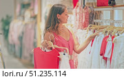 Young woman standing in summer dress in shop and choosing clothes. Shopper looking at rails with white and red clothes in a stylish boutique. Стоковое видео, видеограф Яков Филимонов / Фотобанк Лори