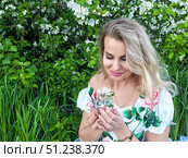 Mature blonde woman enjoys a moment in nature while holding flowers in a lush garden on a sunny day. Стоковое фото, фотограф Кривошеина Елена Леонидовна / Фотобанк Лори