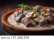 Meat and mushrooms. Dish of stir-fried beef fillet and mushrooms in a creamy thick sauce, served on an iron plate on a wooden board, close-up view. Gourmet food. Beef stroganoff large pieces. Stir Fry. Стоковое AI-изображение, AI-художник Марина Демидюк / Фотобанк Лори