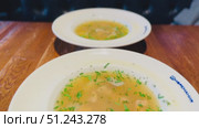 A Truly Delicious Bowl of Soup Elegantly Presented on a Rustic Wooden Table Surface. A warm bowl of savory soup, garnished with herbs, served on a rustic table in a cozy, inviting setting. Стоковое видео, видеограф worker / Фотобанк Лори