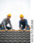 Two smiling roofers working together on a rooftop, teamwork spirit. Стоковое AI-изображение, AI-художник Ольга Невская / Фотобанк Лори
