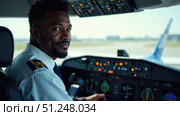 African-American airline captain in cockpit with headset on. Authoritative yet approachable expression with text space for safety instructions or promotions. Стоковое AI-изображение, AI-художник Светлана Леуто / Фотобанк Лори