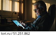 Senior businessman using stylus on tablet, working late in home office. Стоковое фото, фотограф David Kashakhi / Фотобанк Лори