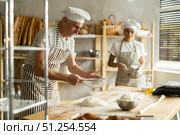 Working in bakery - two bakers whisk eggs and sprinkle flour onto dough through sieve. Стоковое фото, фотограф Татьяна Яцевич / Фотобанк Лори