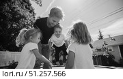 Children playing joyfully on a trampoline with a smiling adult in a backyard on a sunny day. Стоковое AI-изображение, AI-художник Сергей Толмачёв / Фотобанк Лори