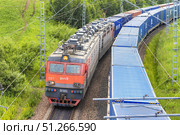 Russia, Krasnoyarsk , 06 07 2024: Freight train VL - 85 of Russian Railways with sea containers travels parallel with another freight train with containers close-up view among green hills. Редакционное фото, фотограф Владимир Разгуляев / Фотобанк Лори