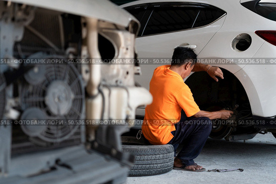 A auto mechanic checking the condition of a car’s brake discs and the condition of the tires that have been used for a while. Стоковое фото, агентство Ingram Publishing / Фотобанк Лори