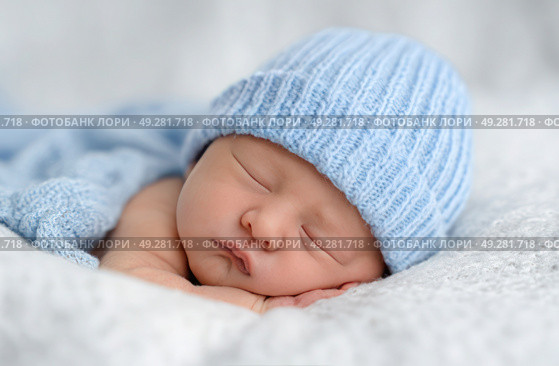 A baby is sleeping with a blue knit hat on. Стоковое AI-изображение, AI-художник Ярославский Максим / Фотобанк Лори