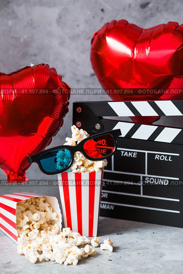 A banner for the film industry. A romantic movie date. A movie camera, 3D glasses, popcorn and foil balloons in the shape of hearts on a concrete gray background. The film will premiere on Valentine's Day. (2024 год). Стоковое фото, фотограф Photojuli / Фотобанк Лори