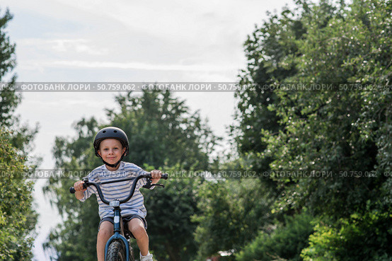 A beautiful 6-year-old boy riding a bicycle in a protective helmet outside. A happy child engaged in an active sport. Protection. Life insurance and child safety. Стоковое фото, фотограф Photojuli / Фотобанк Лори