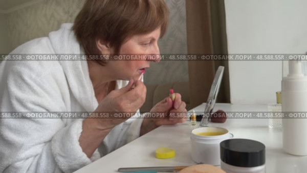 A beautiful senior woman is sitting at home and doing her make-up morning routine. Senior woman putting blush on her face. Стоковое видео, видеограф Ирина Старикова / Фотобанк Лори