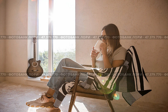 A beautiful woman in a retro armchair, with a mug of hot coffee in the rays of the setting sun. The girl inhales the aroma of the drink. Romance, comfort and harmony. Стоковое фото, фотограф Photojuli / Фотобанк Лори