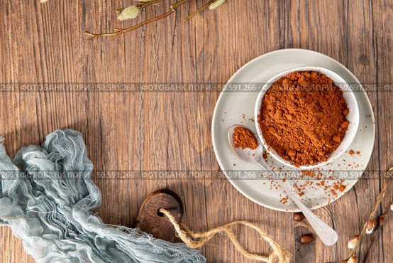 A bowl of rich cocoa powder sits on a wooden table, accompanied by a spoon, perfect for adding a touch of chocolatey goodness to your favorite recipes. Стоковое фото, агентство Ingram Publishing / Фотобанк Лори