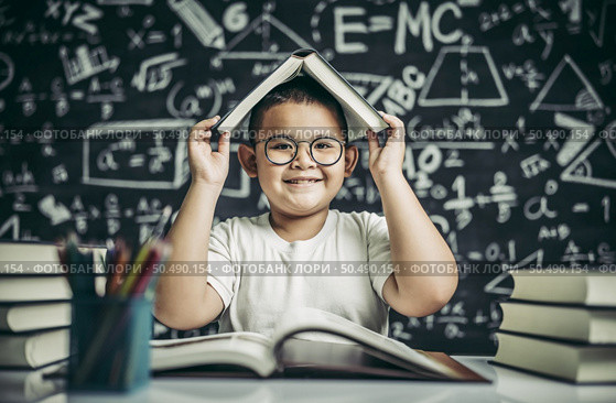 A boy with glasses studied and put a book on his head in the classroom. Стоковое фото, агентство Ingram Publishing / Фотобанк Лори