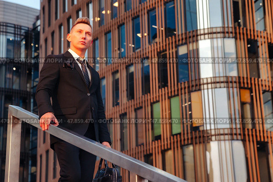 A businessman stands on a staircase, gazing thoughtfully into the distance. The contemporary architecture reflects the warm glow of the evening sun, creating an inspiring atmosphere for ambition. Стоковое фото, фотограф Aleksandr Golubev / Фотобанк Лори