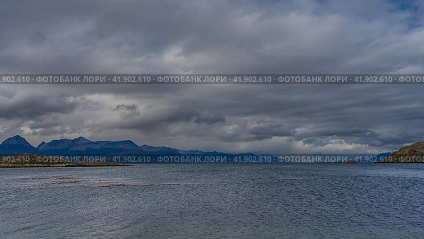 A calm seascape. Islets in the Beagle Channel. Ripples on the ocean surface. Mountains against a background of blue sky and clouds. Argentina. Tierra del Fuego Archipelago (2023 год). Стоковое фото, фотограф Вера Ивановна Кубарева / Фотобанк Лори