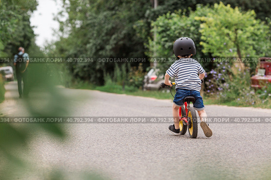 A cheerful little boy rides a running bike in a helmet outdoors. A happy child is engaged in an active sport. Protection. Life insurance and child safety. Стоковое фото, фотограф Photojuli / Фотобанк Лори
