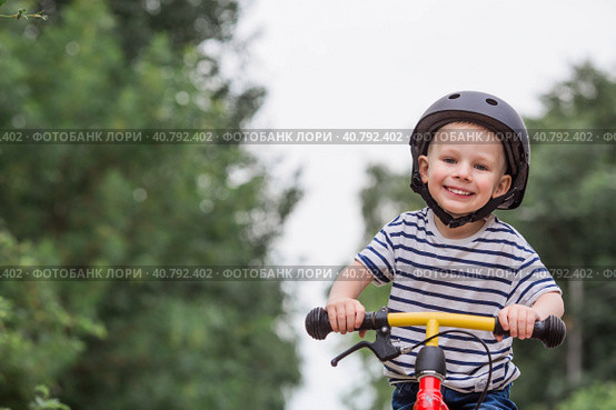 A cheerful little boy rides a running bike in a helmet outdoors. A happy child is engaged in an active sport. Protection. Life insurance and child safety. Стоковое фото, фотограф Photojuli / Фотобанк Лори