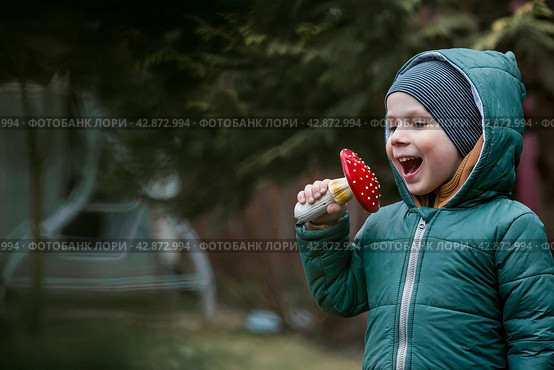 A child and a fly agaric. The boy with the fly agaric. A dangerous poisonous mushroom in the hands of a child. Mushroom poisoning, microdosing, eating herbal medicine. Стоковое фото, фотограф Photojuli / Фотобанк Лори