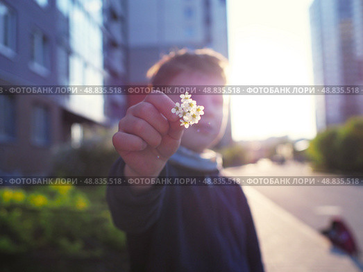 A child gives a flower in a green yard of a multi-story building. Стоковое фото, фотограф Елизавета Малкова / Фотобанк Лори