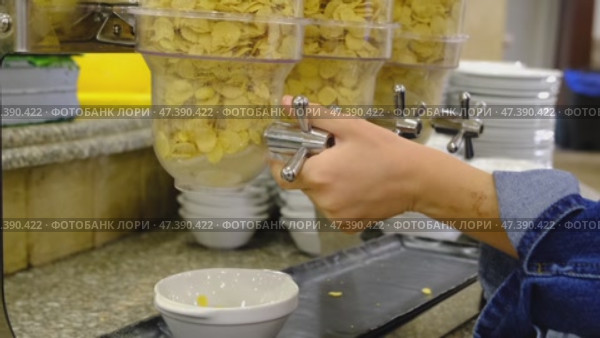 A child's hand pours cornflakes into a breakfast plate on an all-inclusive buffet in the hotel restaurant, turns the dispenser valve. Стоковое видео, видеограф Ольга Симонова / Фотобанк Лори