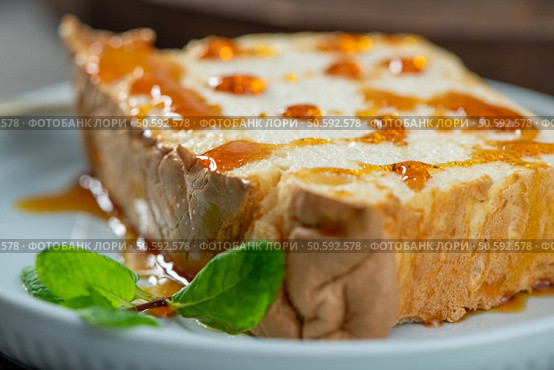 A close-up captures a single slice of molotof, a traditional pudding made from caramelized egg whites, generously drizzled with sweet amber syrup and garnished with bright green mint leaves on a soft blue plate. Стоковое фото, агентство Ingram Publishing / Фотобанк Лори